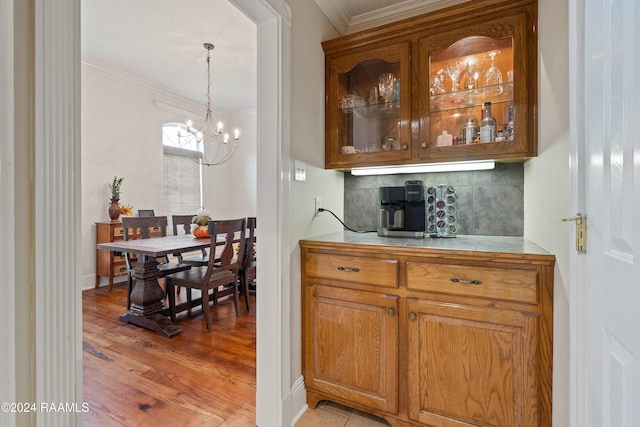 kitchen featuring ornamental molding, tasteful backsplash, hanging light fixtures, a chandelier, and light hardwood / wood-style flooring