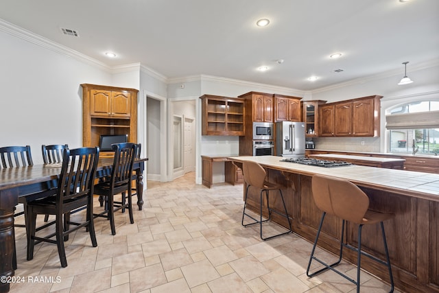 kitchen featuring tile countertops, appliances with stainless steel finishes, a kitchen bar, and ornamental molding