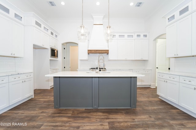 kitchen featuring arched walkways, dark wood-type flooring, stainless steel microwave, and ornamental molding