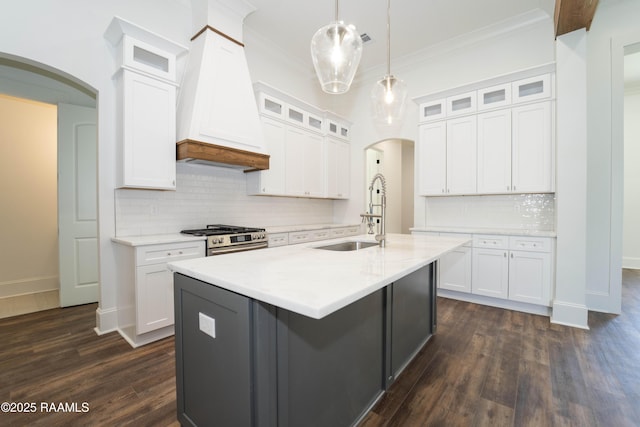 kitchen featuring arched walkways, a sink, white cabinets, gas stove, and custom range hood