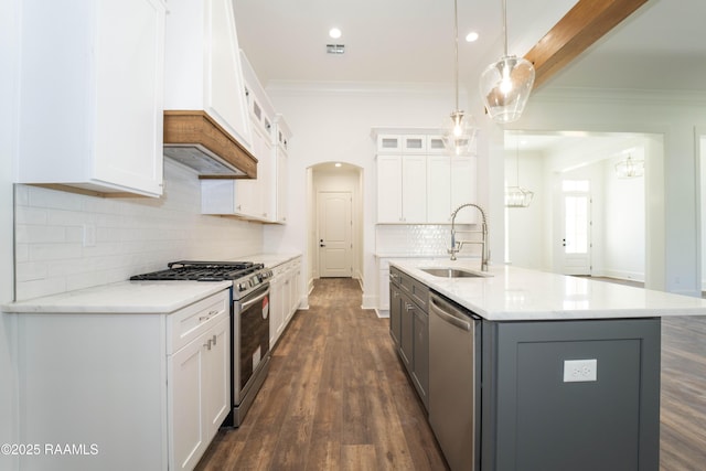 kitchen with arched walkways, stainless steel appliances, a sink, glass insert cabinets, and crown molding