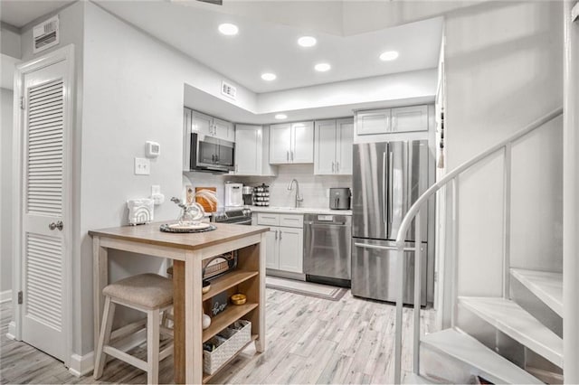 kitchen with recessed lighting, light countertops, light wood-style flooring, backsplash, and appliances with stainless steel finishes