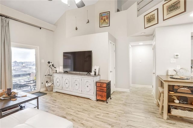 living room featuring light wood-style flooring, high vaulted ceiling, and baseboards