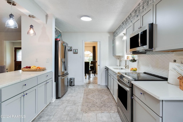 kitchen featuring tasteful backsplash, light stone counters, a textured ceiling, stainless steel appliances, and hanging light fixtures