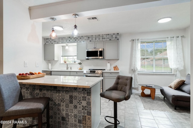 kitchen with a breakfast bar, gray cabinets, decorative light fixtures, kitchen peninsula, and stainless steel appliances