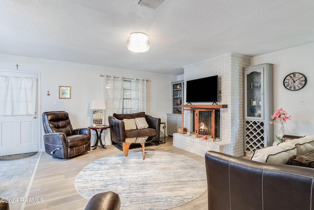 living room featuring a brick fireplace, a textured ceiling, and light hardwood / wood-style flooring