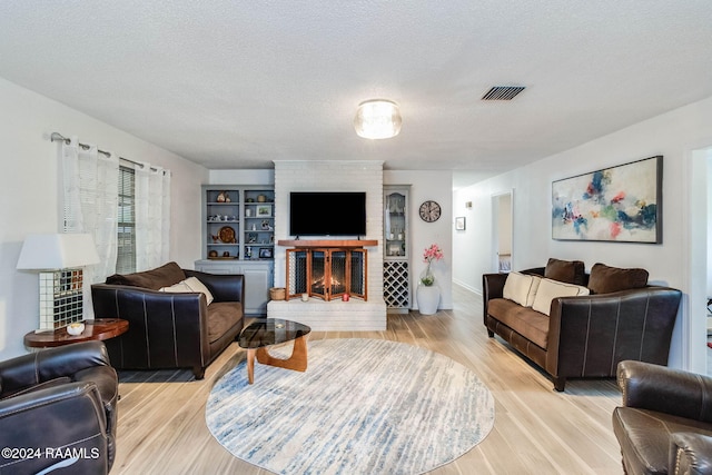 living room with a fireplace, a textured ceiling, and light wood-type flooring