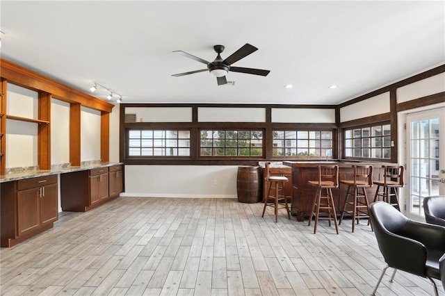 kitchen featuring baseboards, a kitchen breakfast bar, light wood-type flooring, light stone countertops, and track lighting