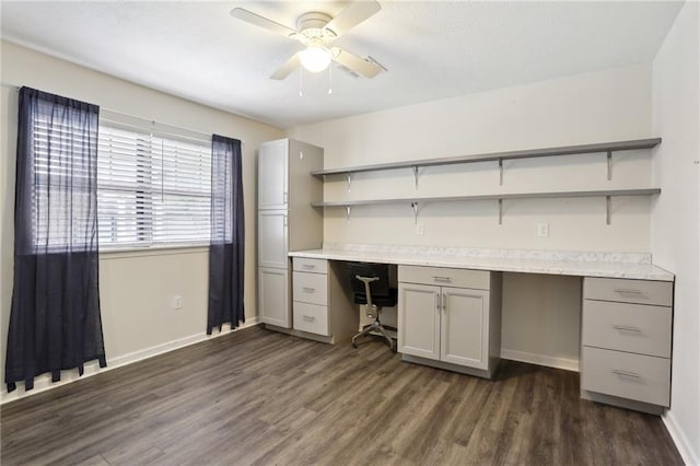 unfurnished office featuring ceiling fan, baseboards, dark wood-type flooring, and built in study area