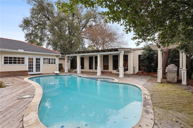 pool with grilling area, a deck, a pergola, and french doors