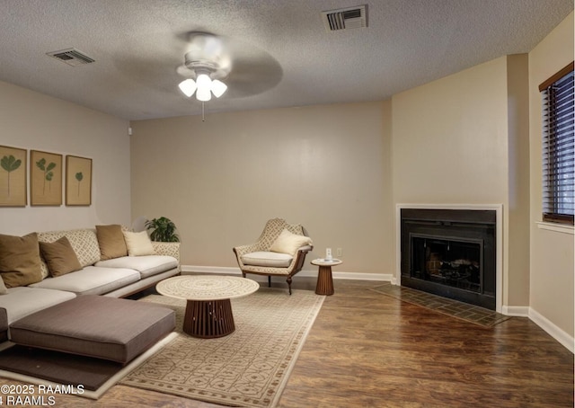 living area with a fireplace with flush hearth, wood finished floors, visible vents, and a textured ceiling