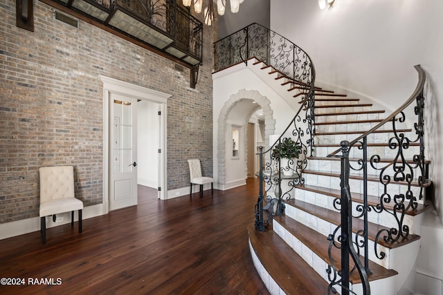 stairs featuring a high ceiling, hardwood / wood-style flooring, and brick wall