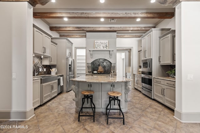 kitchen with beam ceiling, gray cabinets, a kitchen island with sink, and appliances with stainless steel finishes