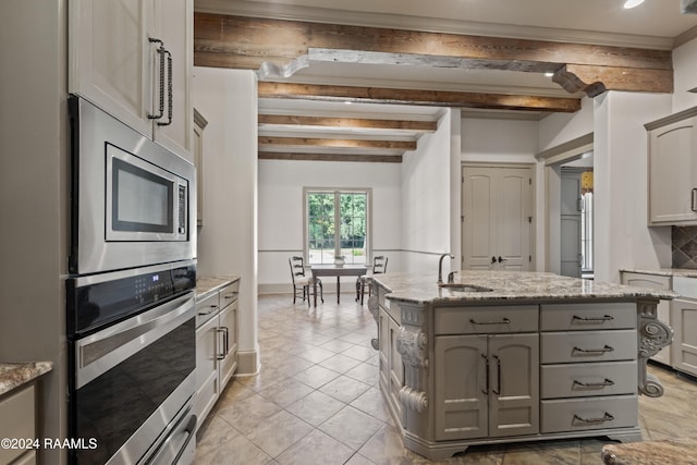 kitchen with beam ceiling, gray cabinetry, sink, tasteful backsplash, and a center island with sink