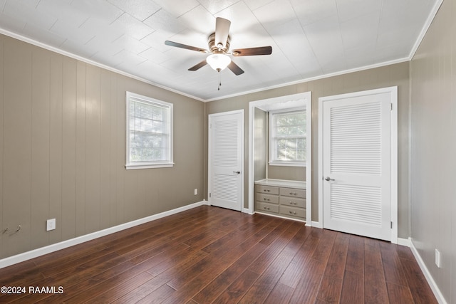 unfurnished bedroom with ceiling fan, crown molding, dark wood-type flooring, and multiple closets