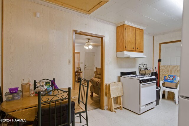 kitchen with wooden walls, white range with gas cooktop, crown molding, and ceiling fan