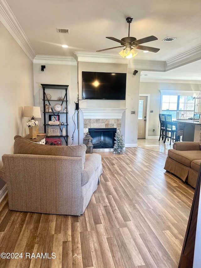 living room with a fireplace, light hardwood / wood-style floors, ceiling fan, and ornamental molding