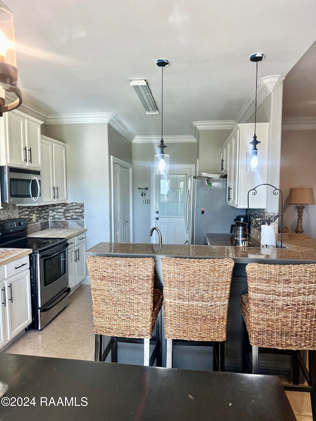 kitchen featuring white cabinetry, stainless steel appliances, pendant lighting, a kitchen bar, and ornamental molding