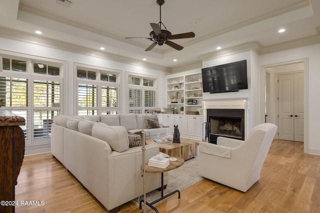 living room with a raised ceiling, light hardwood / wood-style flooring, ceiling fan, and crown molding