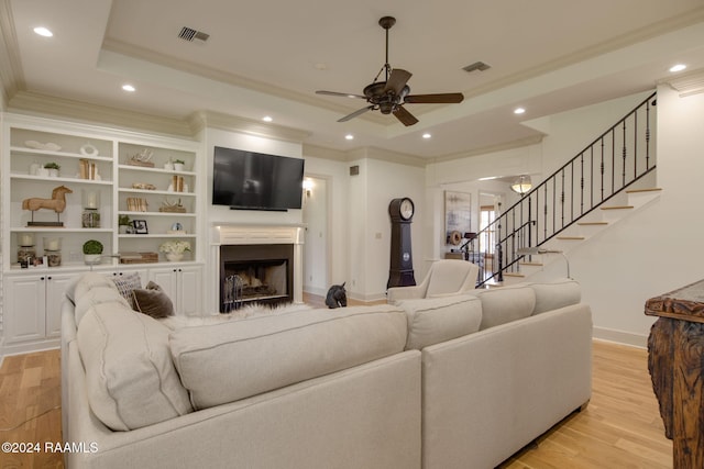 living room with light wood-type flooring, a tray ceiling, ceiling fan, and crown molding