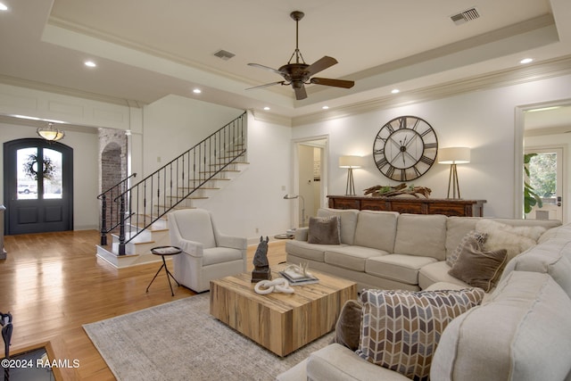 living room with a raised ceiling, crown molding, ceiling fan, and light wood-type flooring