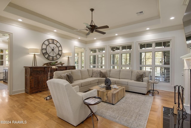 living room with light wood-type flooring, a raised ceiling, ceiling fan, and ornamental molding