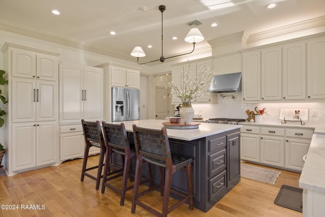 kitchen with stainless steel fridge, extractor fan, decorative light fixtures, a center island, and light hardwood / wood-style floors