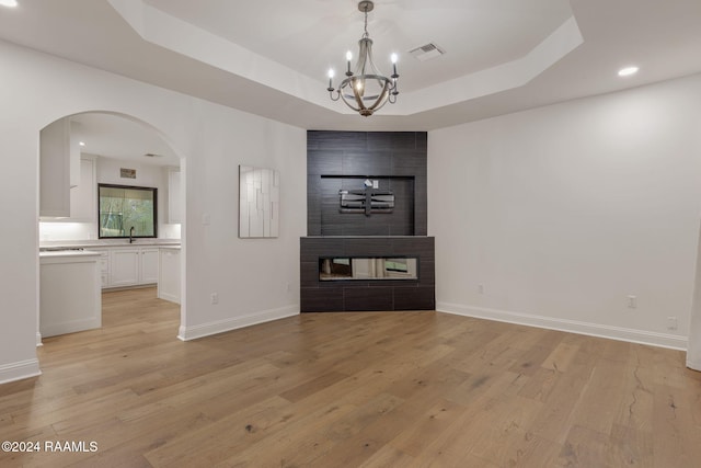 interior space featuring a raised ceiling, a chandelier, light hardwood / wood-style floors, and a multi sided fireplace