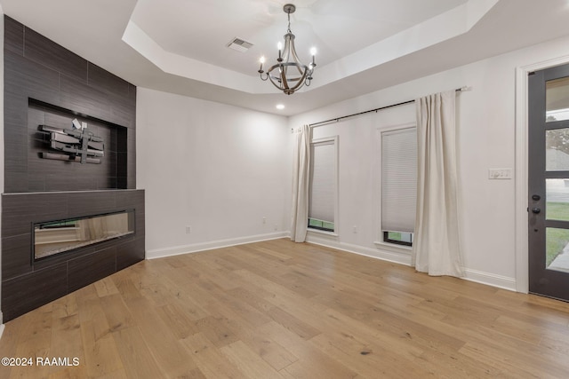 interior space featuring a tile fireplace, light wood-type flooring, an inviting chandelier, and a raised ceiling