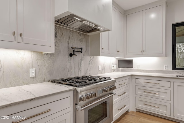 kitchen with white cabinetry, light stone countertops, wall chimney exhaust hood, stainless steel stove, and light wood-type flooring