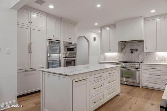 kitchen with custom range hood, light wood-type flooring, white cabinetry, and high quality appliances