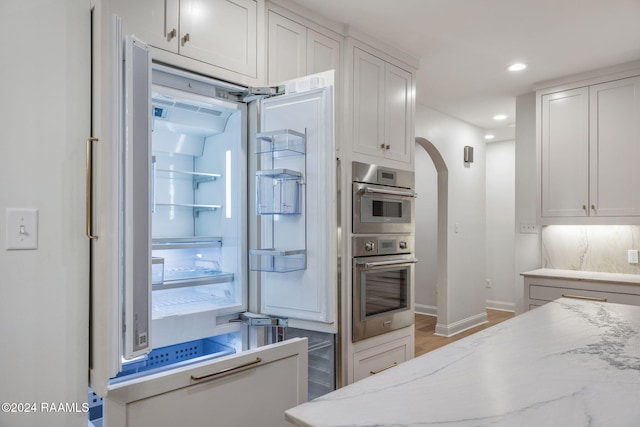 kitchen featuring light stone countertops, built in refrigerator, hardwood / wood-style flooring, and white cabinetry