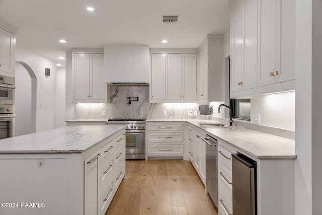 kitchen featuring light wood-type flooring, custom range hood, stainless steel appliances, sink, and white cabinetry