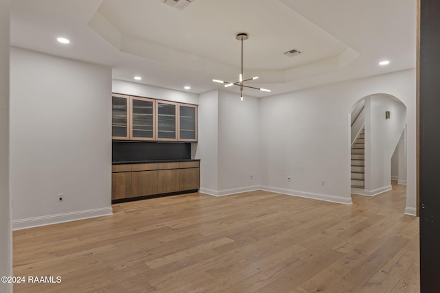 unfurnished living room with light hardwood / wood-style floors, a raised ceiling, and a chandelier