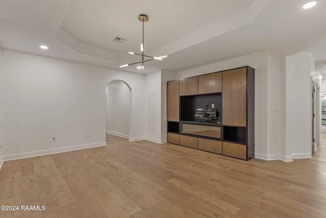 unfurnished living room featuring a raised ceiling, light wood-type flooring, and an inviting chandelier