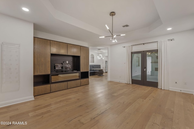 unfurnished living room with a notable chandelier, a raised ceiling, french doors, and light hardwood / wood-style flooring