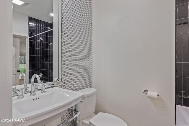 bathroom with a tile shower, sink, and toilet