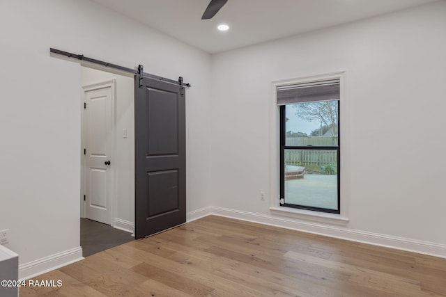 empty room with a barn door, ceiling fan, and wood-type flooring