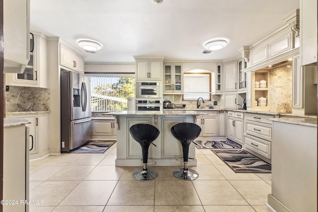 kitchen with a kitchen breakfast bar, light stone countertops, light tile patterned flooring, and stainless steel appliances