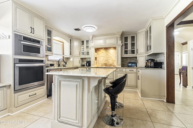 kitchen featuring light tile patterned flooring, a center island, oven, and light stone counters