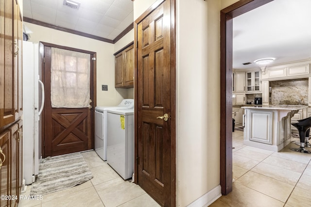 laundry area with cabinets, light tile patterned floors, crown molding, and washing machine and clothes dryer