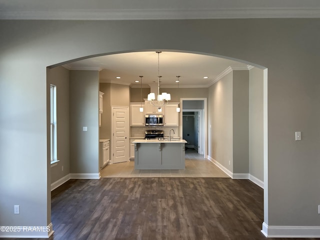 kitchen featuring sink, appliances with stainless steel finishes, white cabinets, a center island with sink, and decorative light fixtures