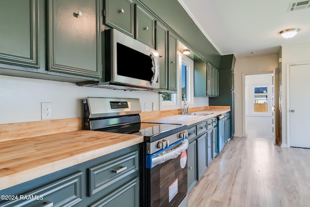 kitchen with stainless steel appliances, wood counters, plenty of natural light, light hardwood / wood-style floors, and green cabinetry