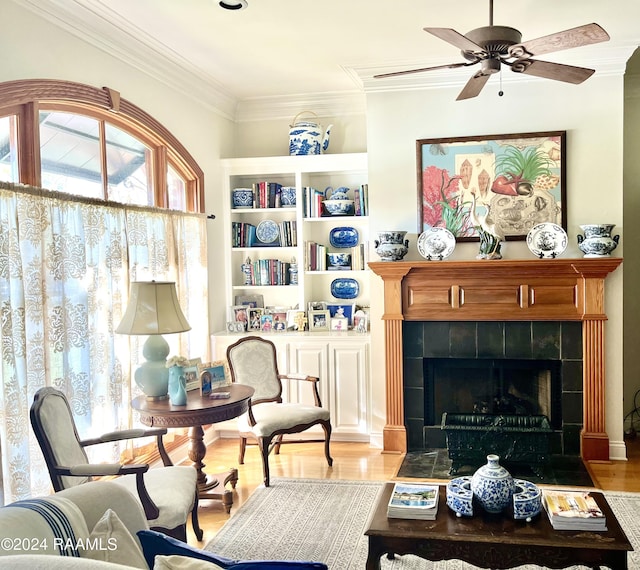 living room featuring a tiled fireplace, ceiling fan, light hardwood / wood-style flooring, and ornamental molding