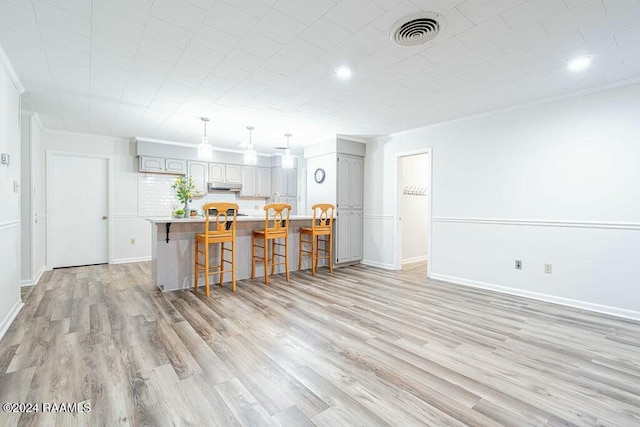 kitchen featuring gray cabinetry, a breakfast bar, crown molding, a kitchen island, and light hardwood / wood-style floors