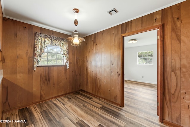 spare room with wooden walls, wood-type flooring, ornamental molding, and a wealth of natural light