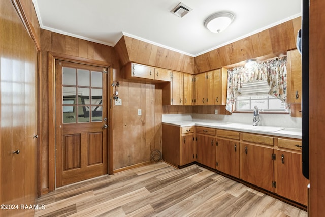 kitchen featuring light wood-type flooring, crown molding, wooden walls, and sink