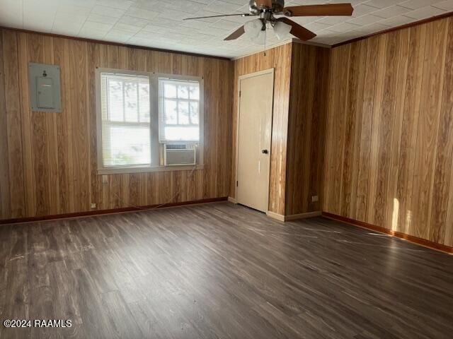 spare room featuring ceiling fan, dark wood-type flooring, electric panel, cooling unit, and wooden walls