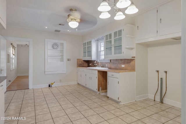 kitchen with sink, pendant lighting, white cabinets, ceiling fan with notable chandelier, and ornamental molding