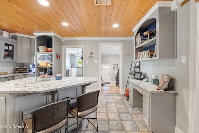 kitchen featuring decorative backsplash, a breakfast bar, gray cabinetry, and wood ceiling